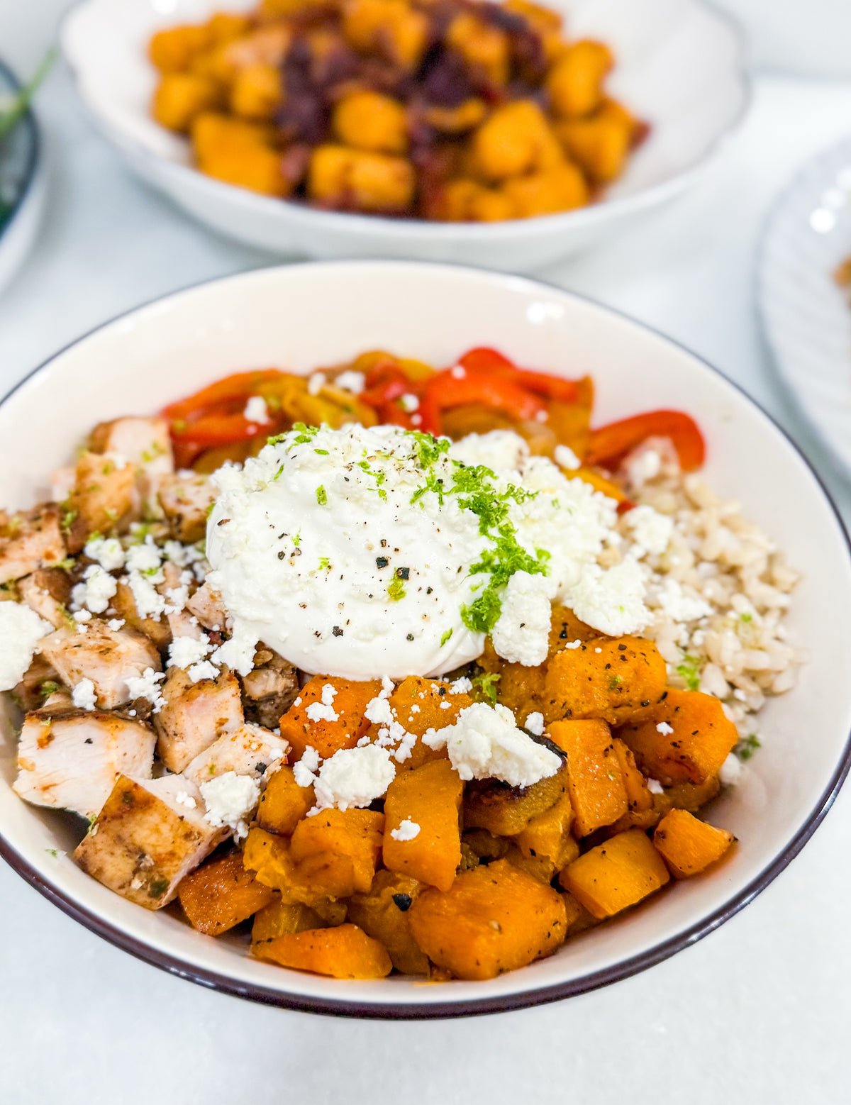 Butternut Squash Fajita Bowl - Roasted butternut squash, bell peppers, caramelized onions, and fajita-spiced chicken over brown rice, finished with lime crema, cotija